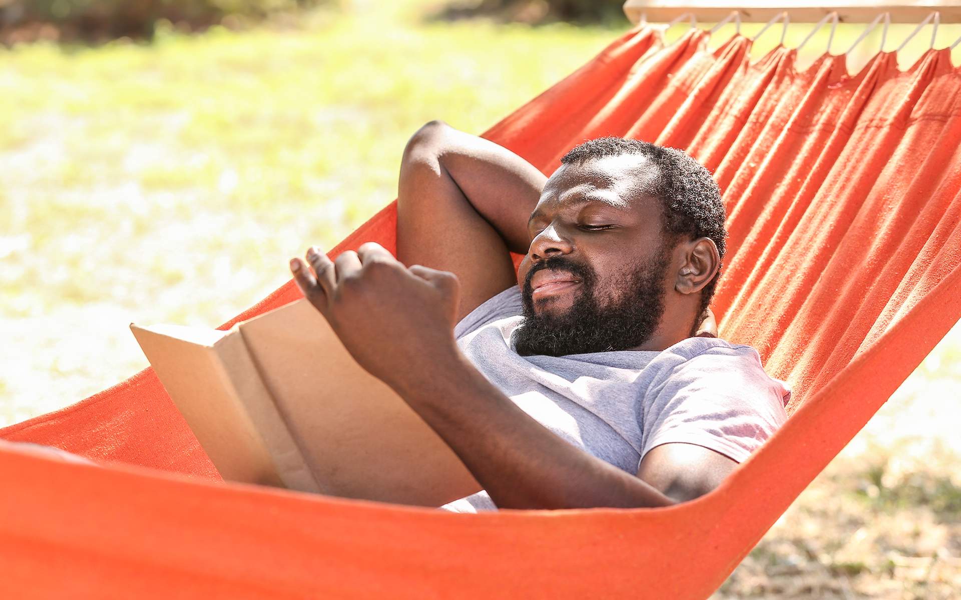 6 Books to Add to Your Summer Reading List - A man reading a book in a hammock