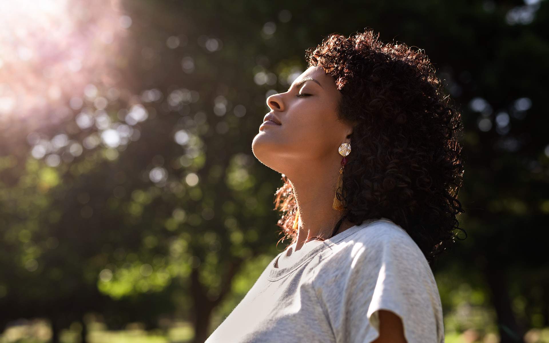Young woman standing with her eyes closed and head raised to the sky in a park on a sunny summer afternoon