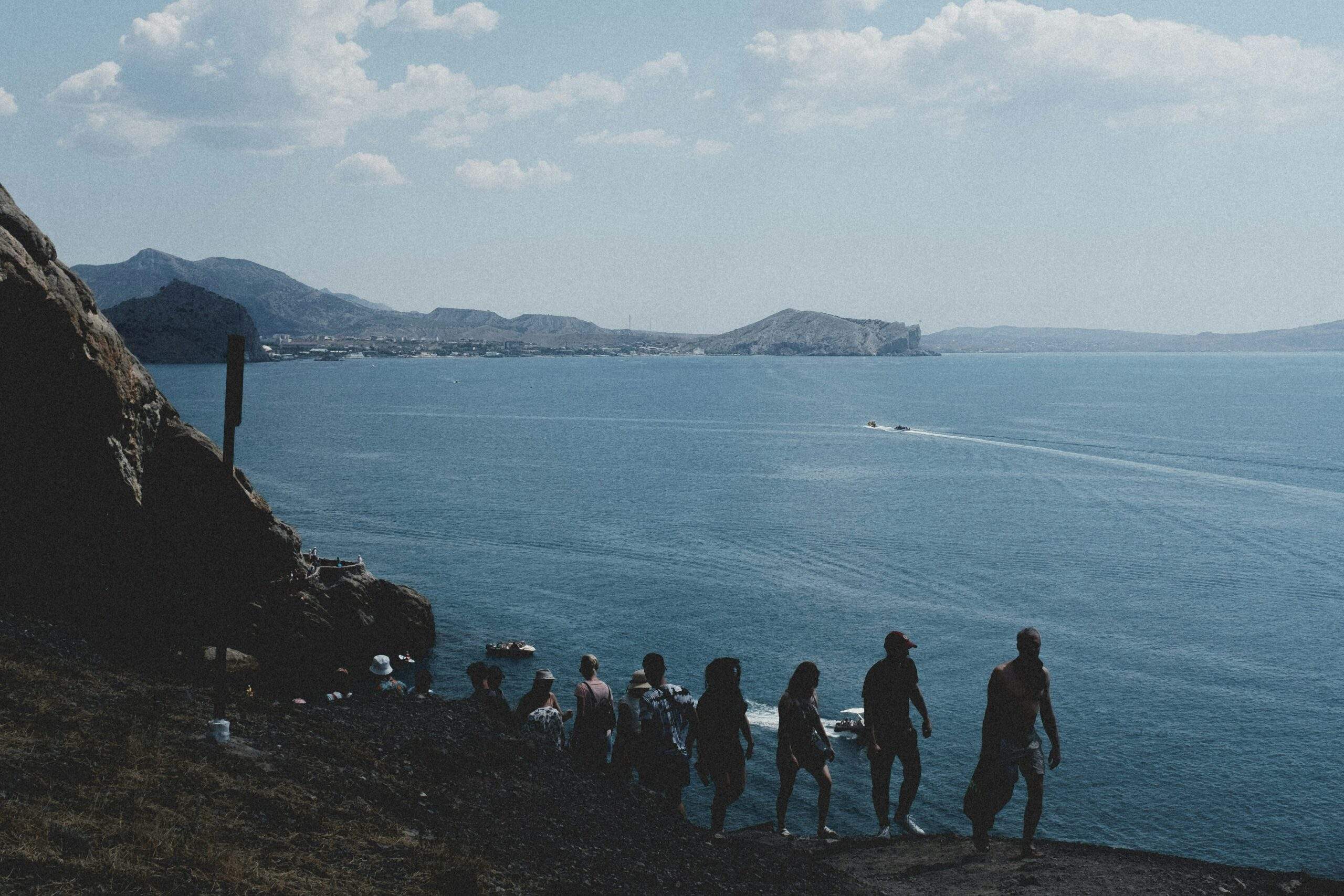 A group of people standing on a clifftop overlooking a blue sea with distant islands.