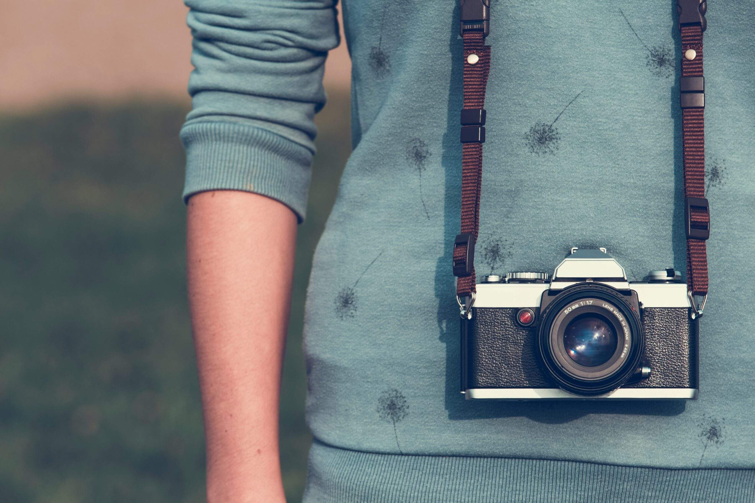 An analog camera hanging around a woman's neck.