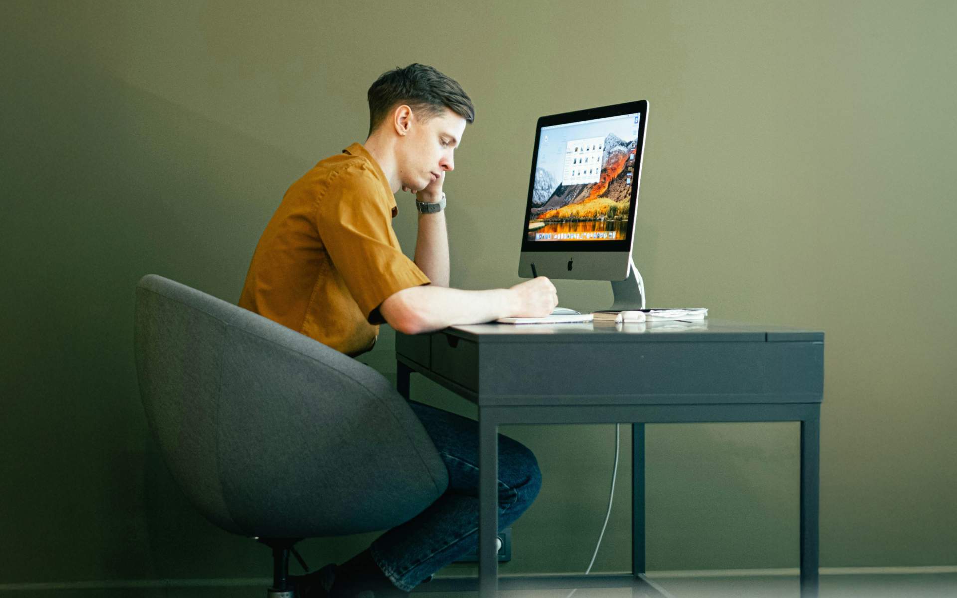 A modern workspace setup showing a person working thoughtfully at a computer, reflecting the importance of wellbeing in today’s digital work environment.