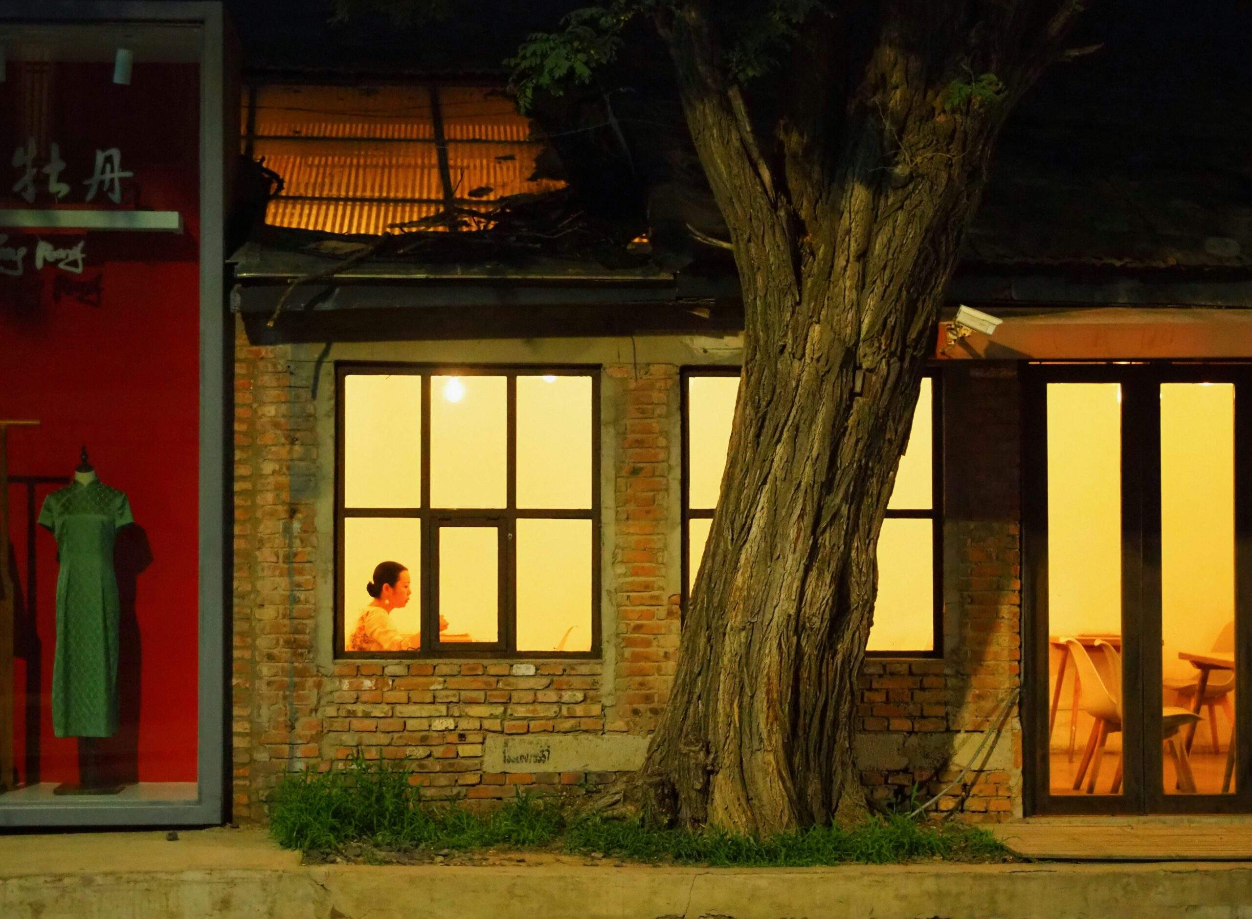A person sitting alone at a table in a warmly lit brick building with large windows at night, inviting the onlooker to slow down.