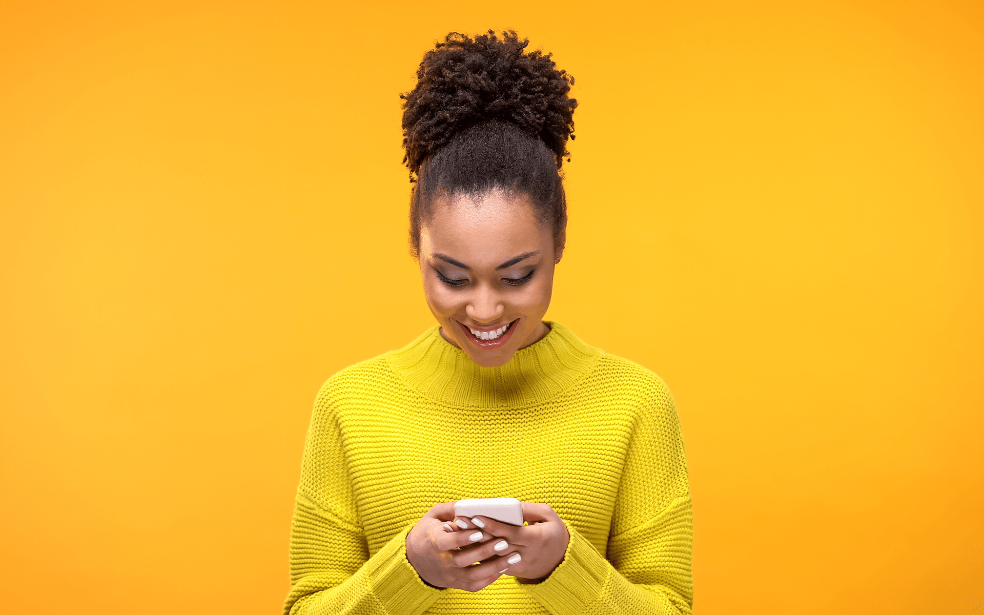 Black woman in a yellow T-shirt smiling down at her meditation subscription with a yellow studio background.