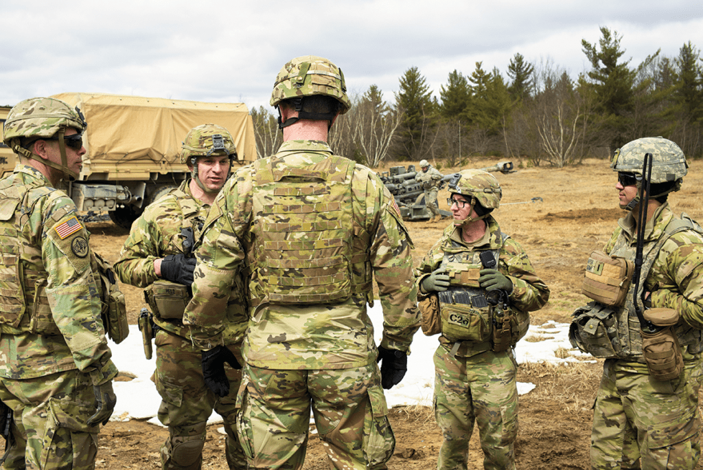 Military personnel in camouflage uniforms conduct a training exercise in an open field.