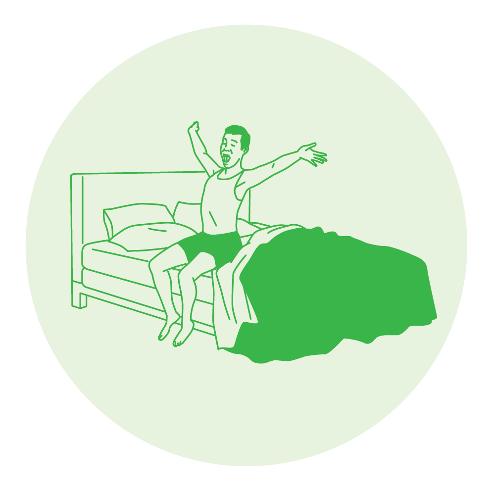 A person sitting on a bed stretching their arms upward with a green blanket on the floor.